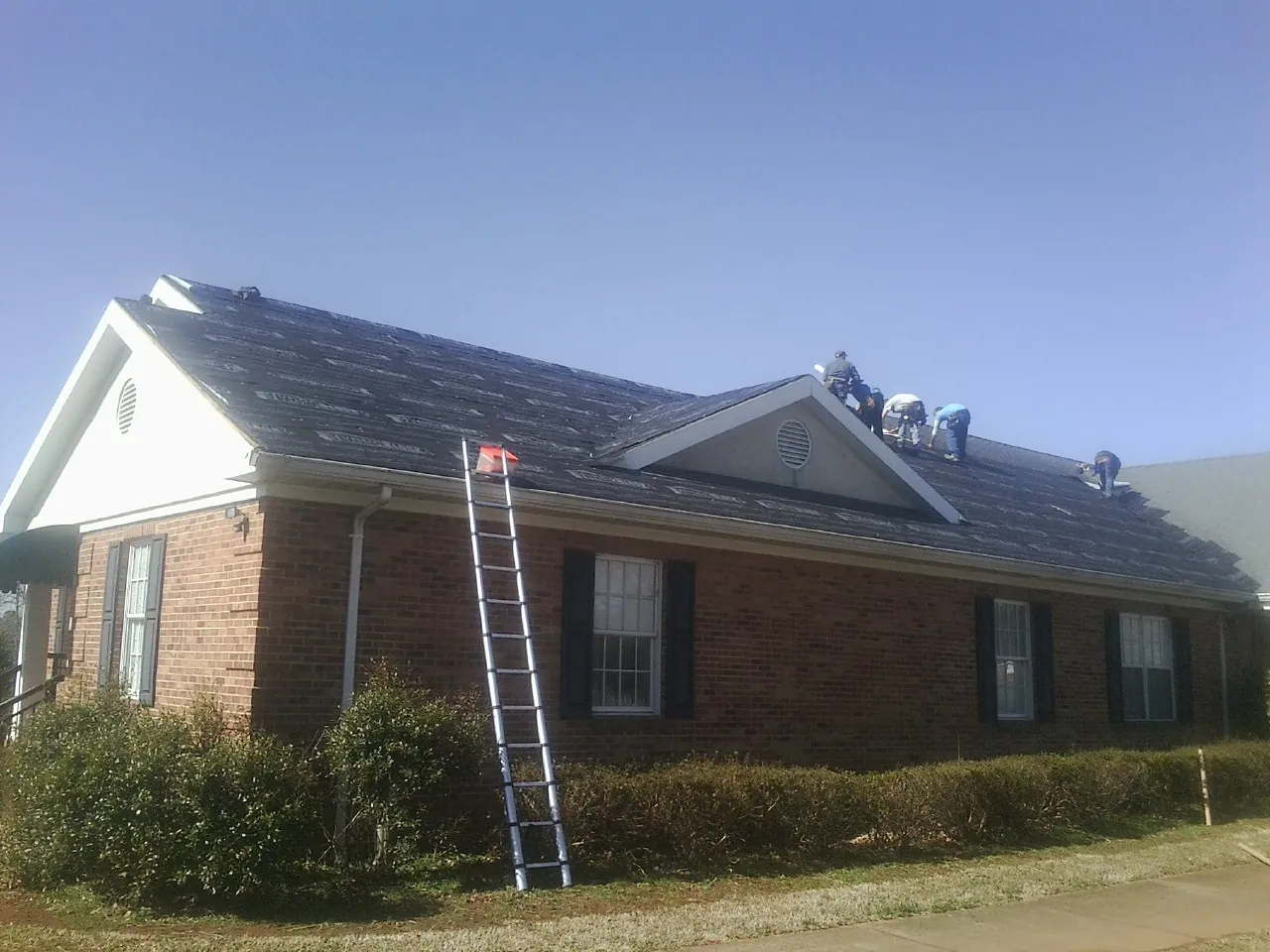 Crew tearing shingles off a brick ranch roof with a ladder set — Emergency Roof Repair work by our crew in Church Creek