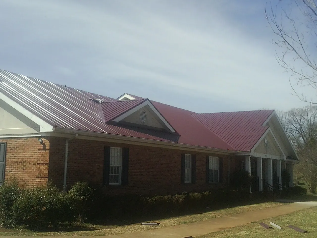 Red metal roof with gabled entries on a long brick building, from a Hail Damage Roof Repair job in Church Creek