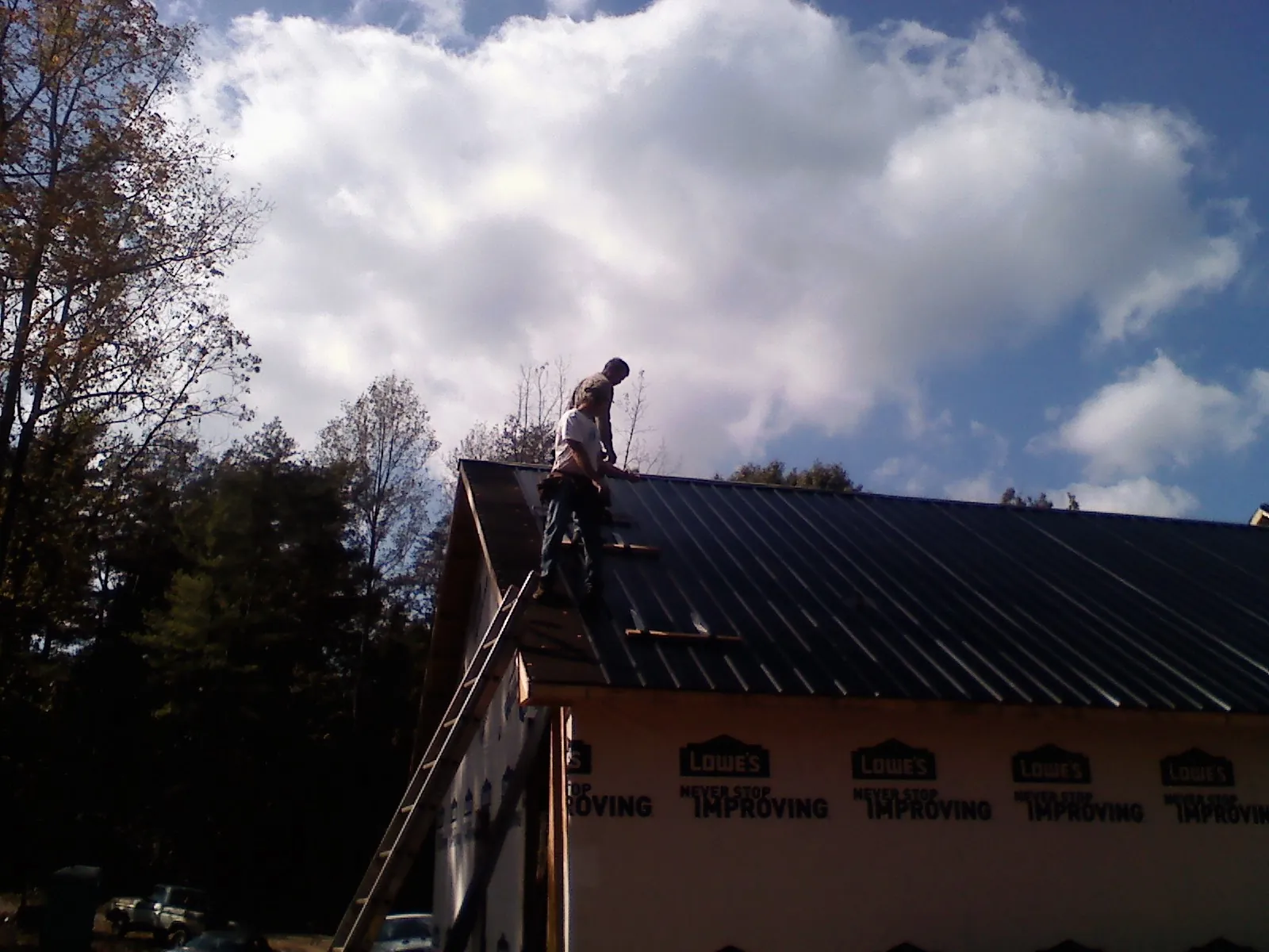 Roofer fastening dark metal panels high against a cloudy sky, from a Roof Inspection job in Church Creek