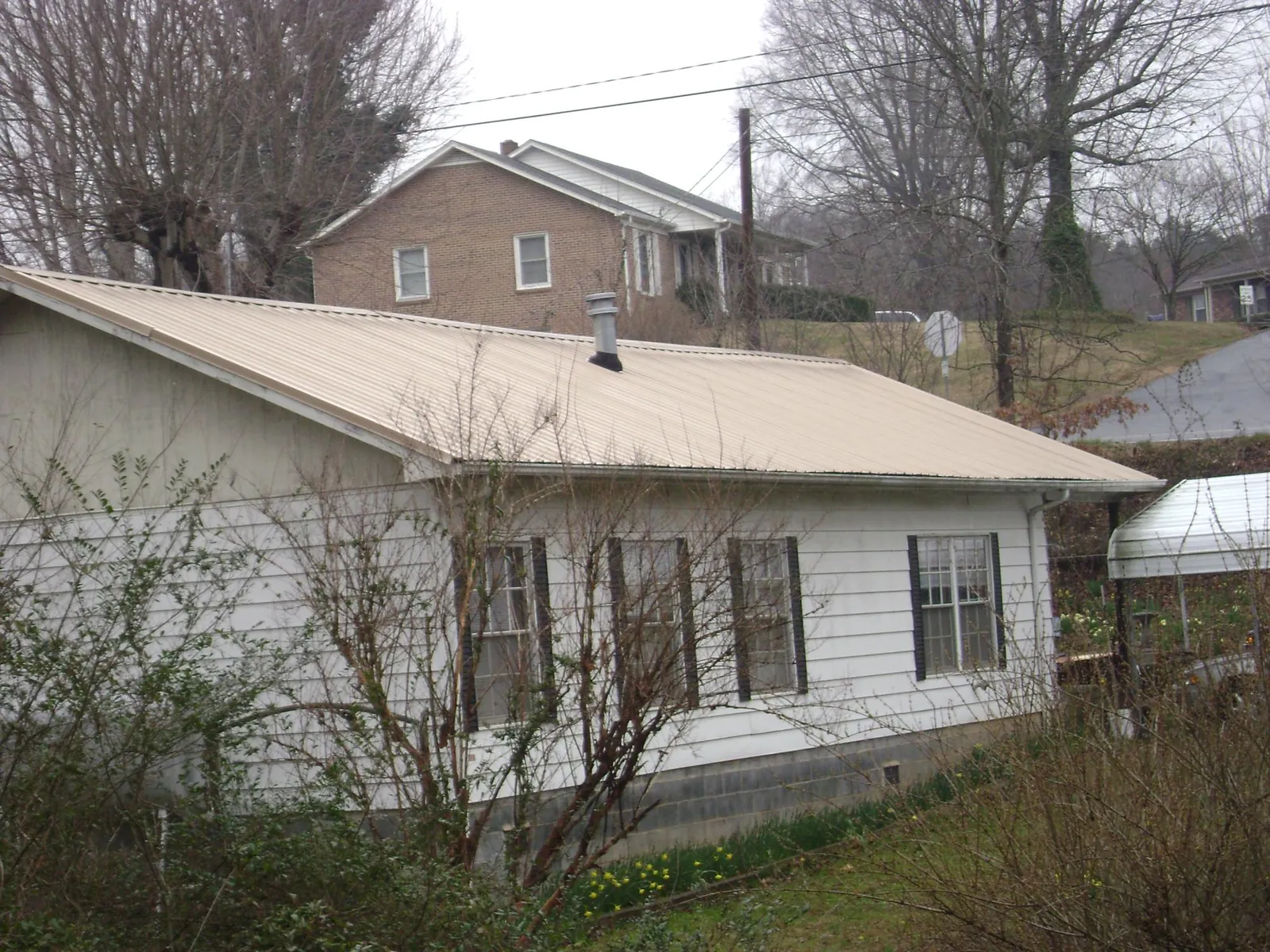 Tan metal roof on a white sided house set into a hillside — Commercial Roofing by Roofing Brothers in Church Creek
